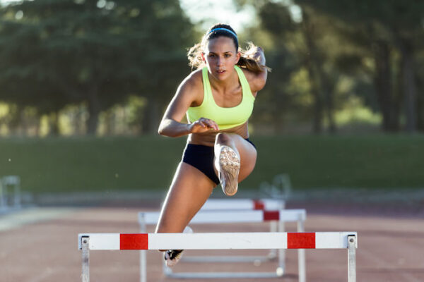 Portrait of young athlete jumping over a hurdle during training on race track