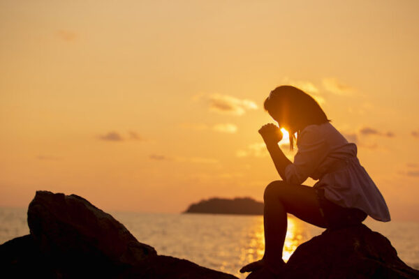 Women praying on beach by ocean at sunset