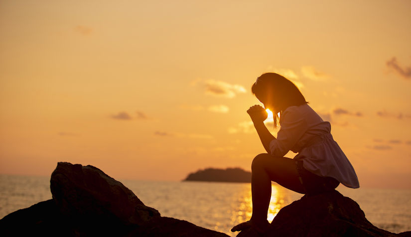 Women praying on beach by ocean at sunset