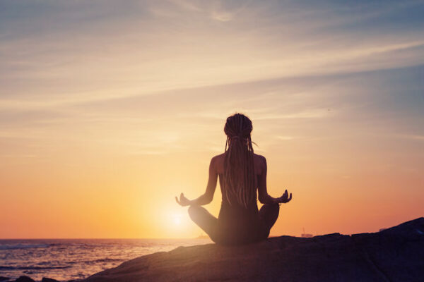 Silhouette of woman sitting back, meditating lotus yoga pose on the beach