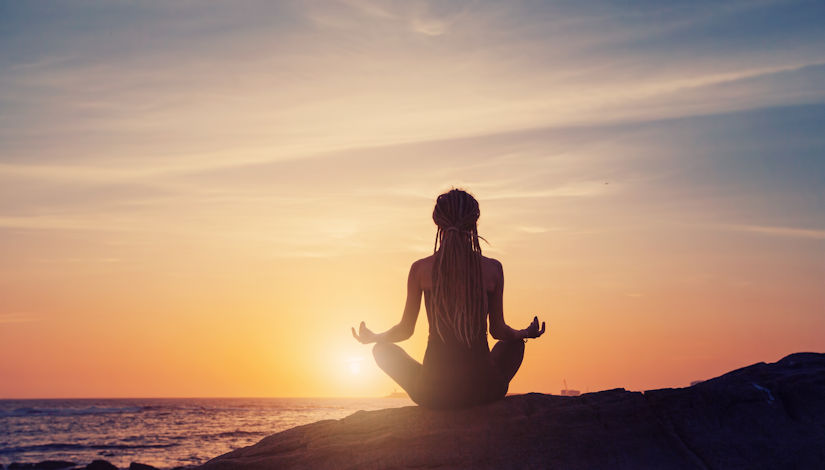 Silhouette of woman sitting back, meditating lotus yoga pose on the beach