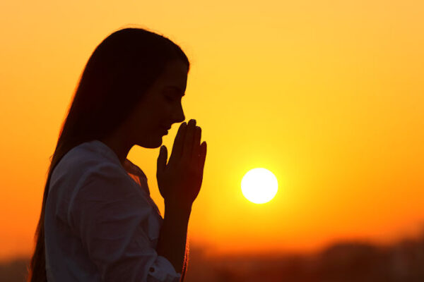 Backlight of a woman praying at sunset