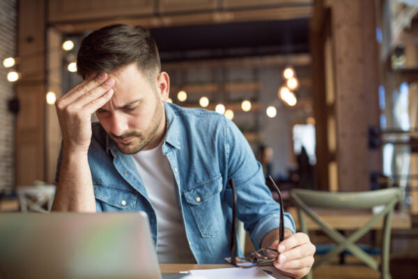 Man looking at laptop with one hand on forehead looking stressed