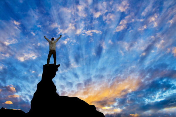 Man standing at sunrise on top of rocks looking at the sky with hands up