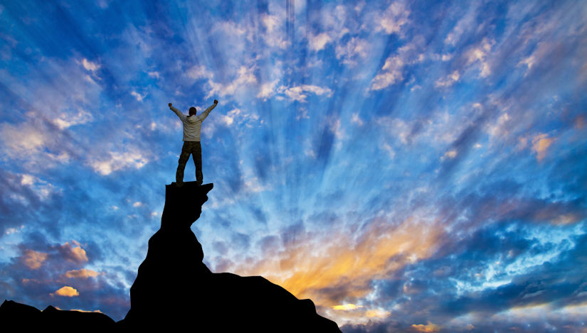 Man standing at sunrise on top of rocks looking at the sky with hands up