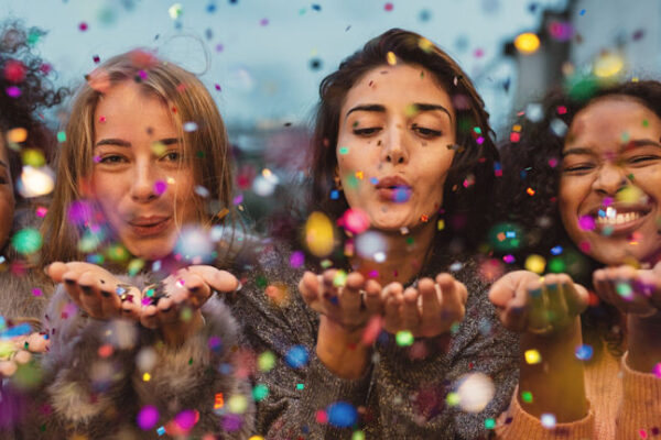 Young women celebrating happy birthday by blowing confetti from hands