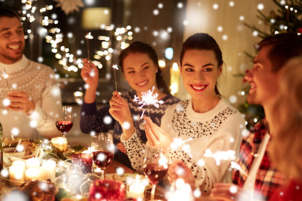 Winter holidays: happy friends with sparklers celebrating at home