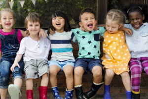 Group of kindergarten friends with their arms around each other while sitting and smiling