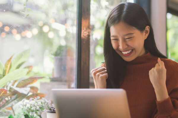 Young woman celebrates work success looking at her laptop